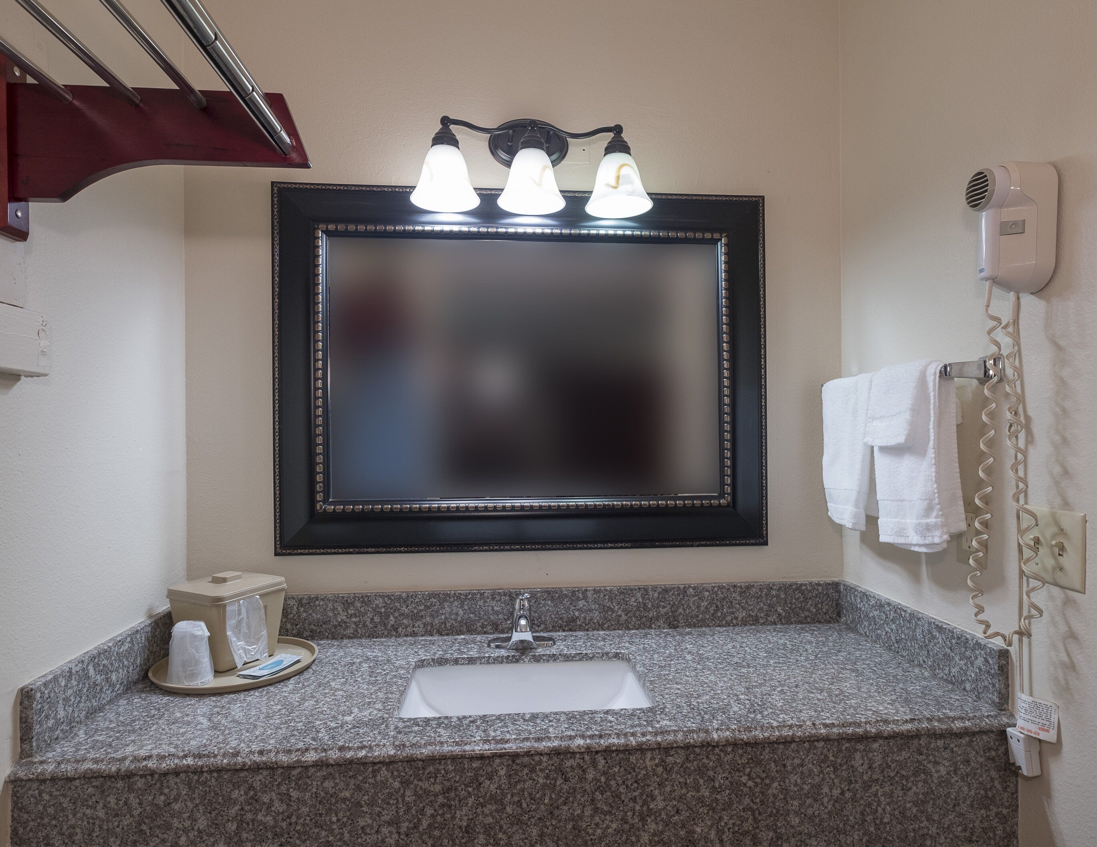 A bathroom with a granite countertop, a sink, a mirror with three lights, and a towel rack.