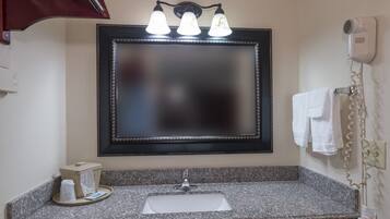A bathroom with a granite countertop, a sink, a mirror with three lights, and a towel rack.