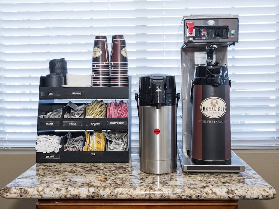 A coffee machine, a stainless steel thermos, and a dispenser with various coffee pods on a countertop.