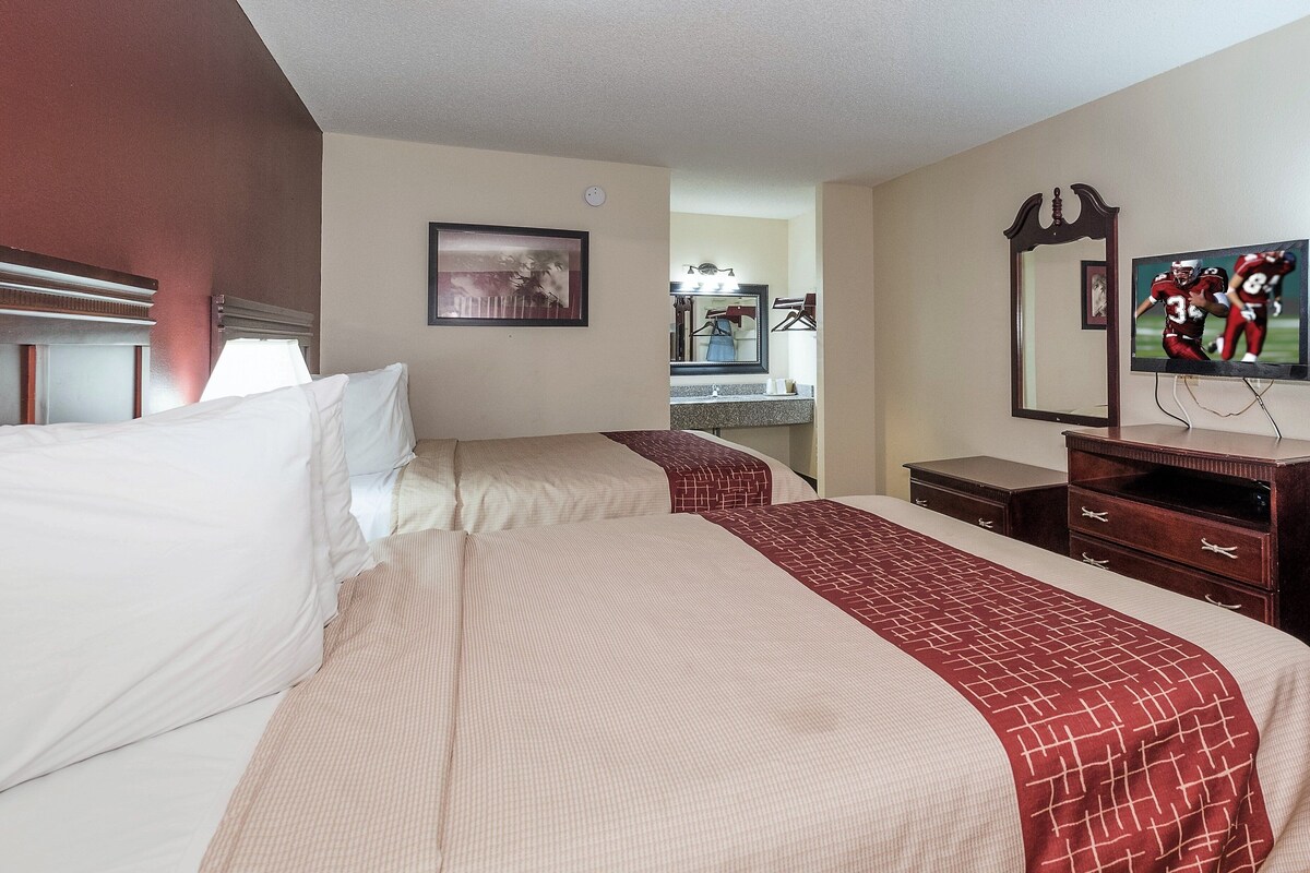 A hotel room with two beds, a dresser, a mirror, and a television.