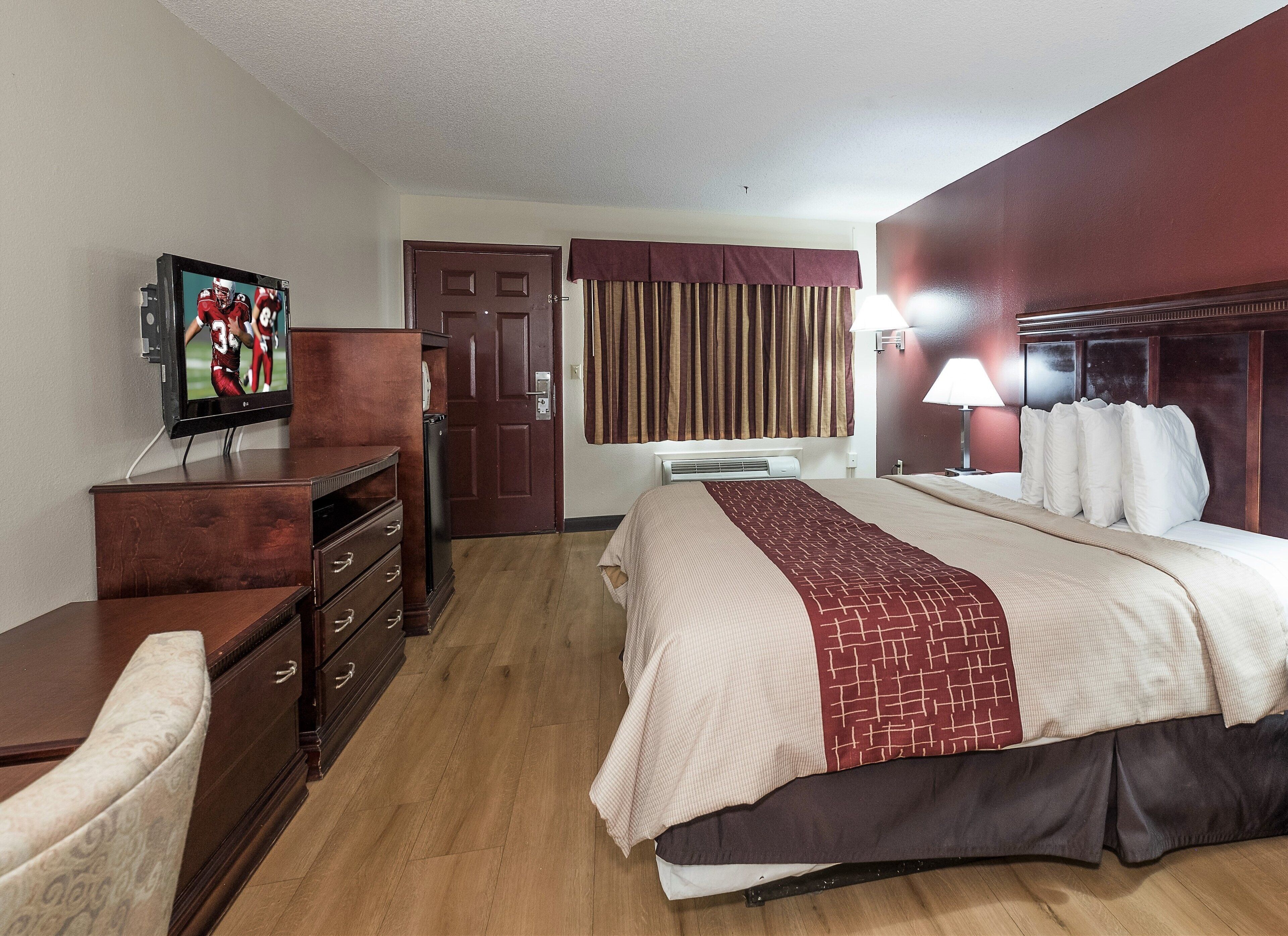 A hotel room with a bed, a television, a dresser, and a door.