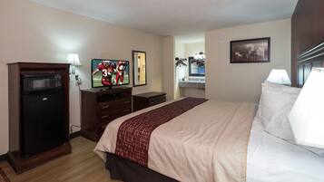 A hotel room with a bed, a TV, a refrigerator, a dresser, a mirror, and a picture on the wall.