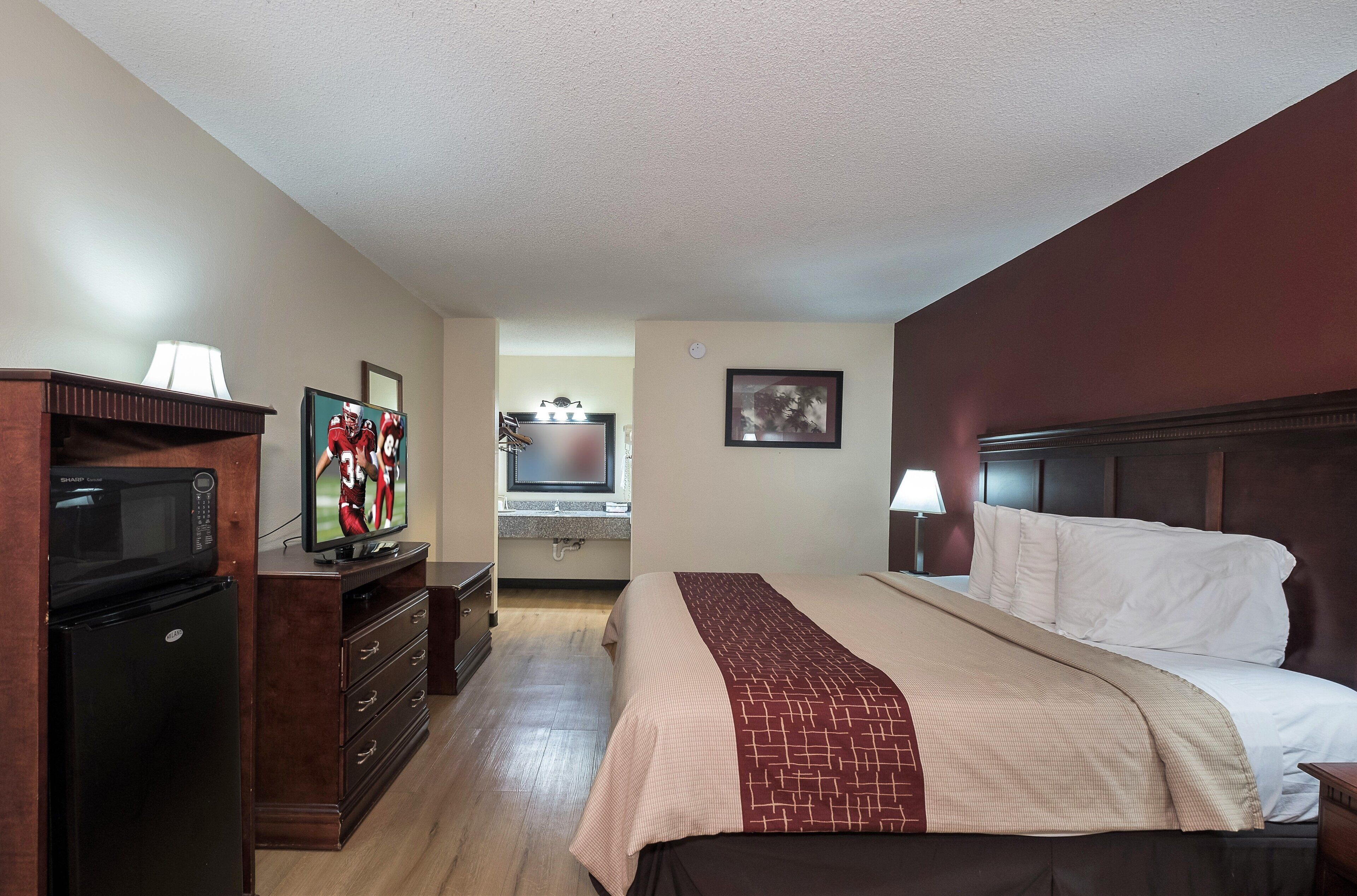A hotel room with a bed, a television, a microwave, a dresser, and a bathroom visible in the background.