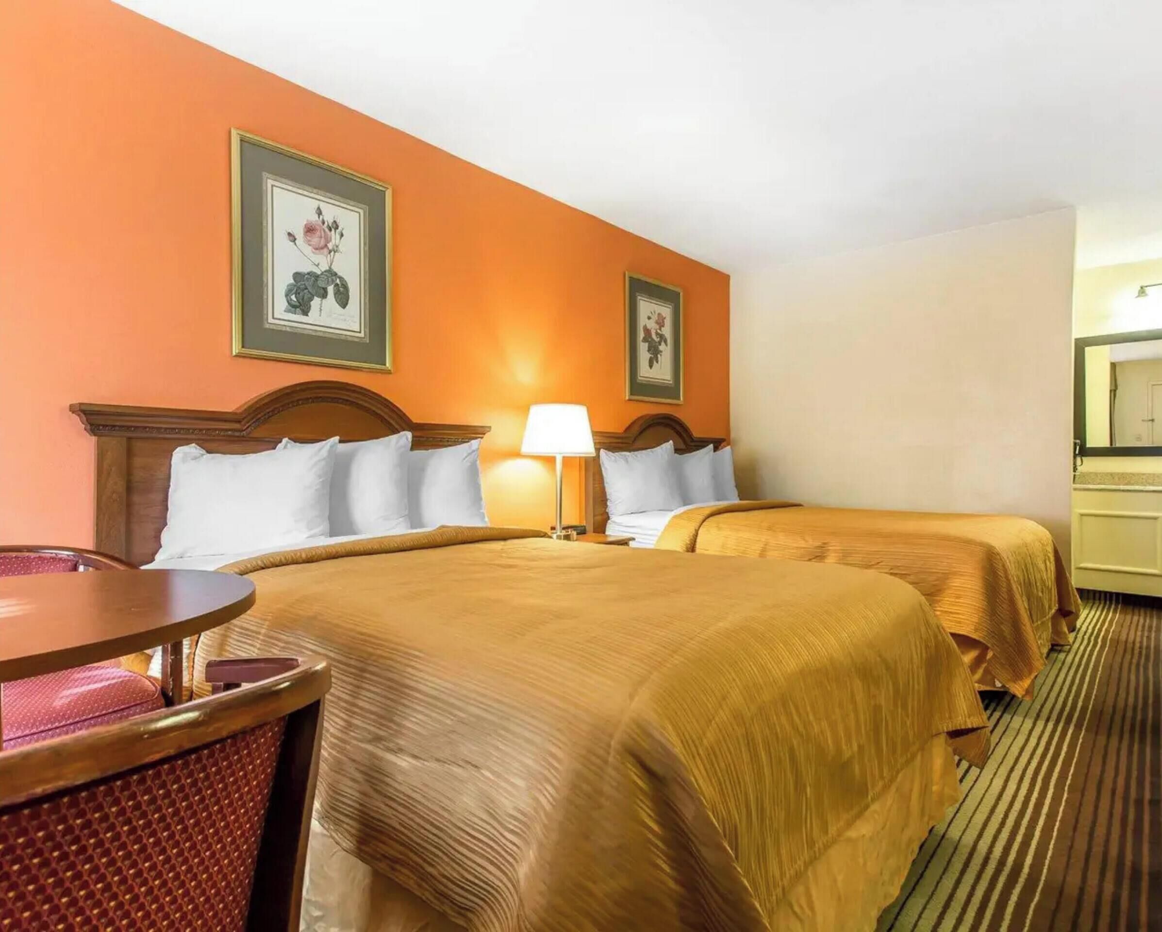 A hotel room with two beds, a round table, and a chair.
