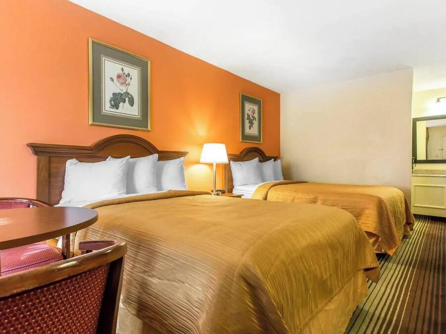 A hotel room with two beds, a round table, and a chair.
