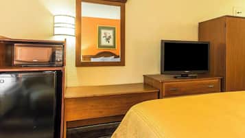 A hotel room with a bed, a television, a microwave, a refrigerator, a wooden dresser, and a mirror.