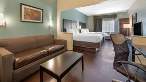 A hotel room with a brown leather sofa, a wooden coffee table, a single bed with white bedding, a desk with a chair, and a TV. - Best Western Hilliard Inn & Suites (Hilliard)