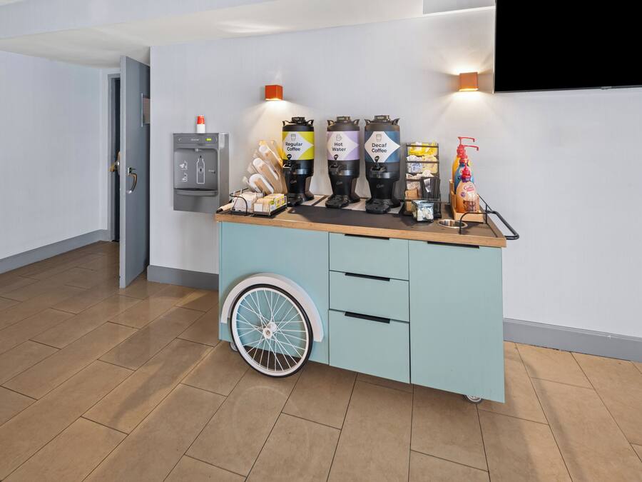 A self-service coffee station with dispensers for regular coffee, hot water, and decaf coffee, a coffee machine, and a bottle of coffee creamer.