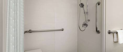 A bathroom with white tiled walls, a shower with a handheld showerhead, a grab bar, and a towel rack.