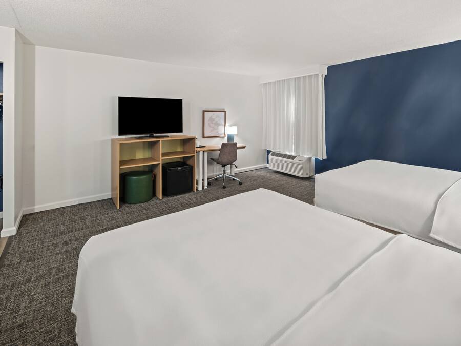 Une chambre d’hôtel avec deux lits, un bureau avec une chaise, une télévision, une lampe et une armoire.