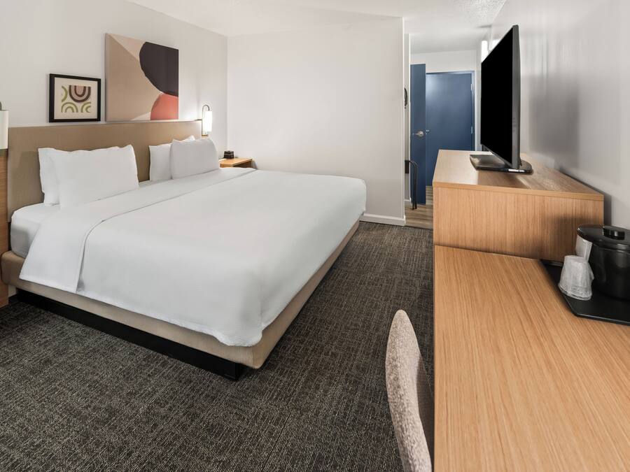 Una habitación de hotel con una cama grande, un escritorio, un televisor y una cafetera.