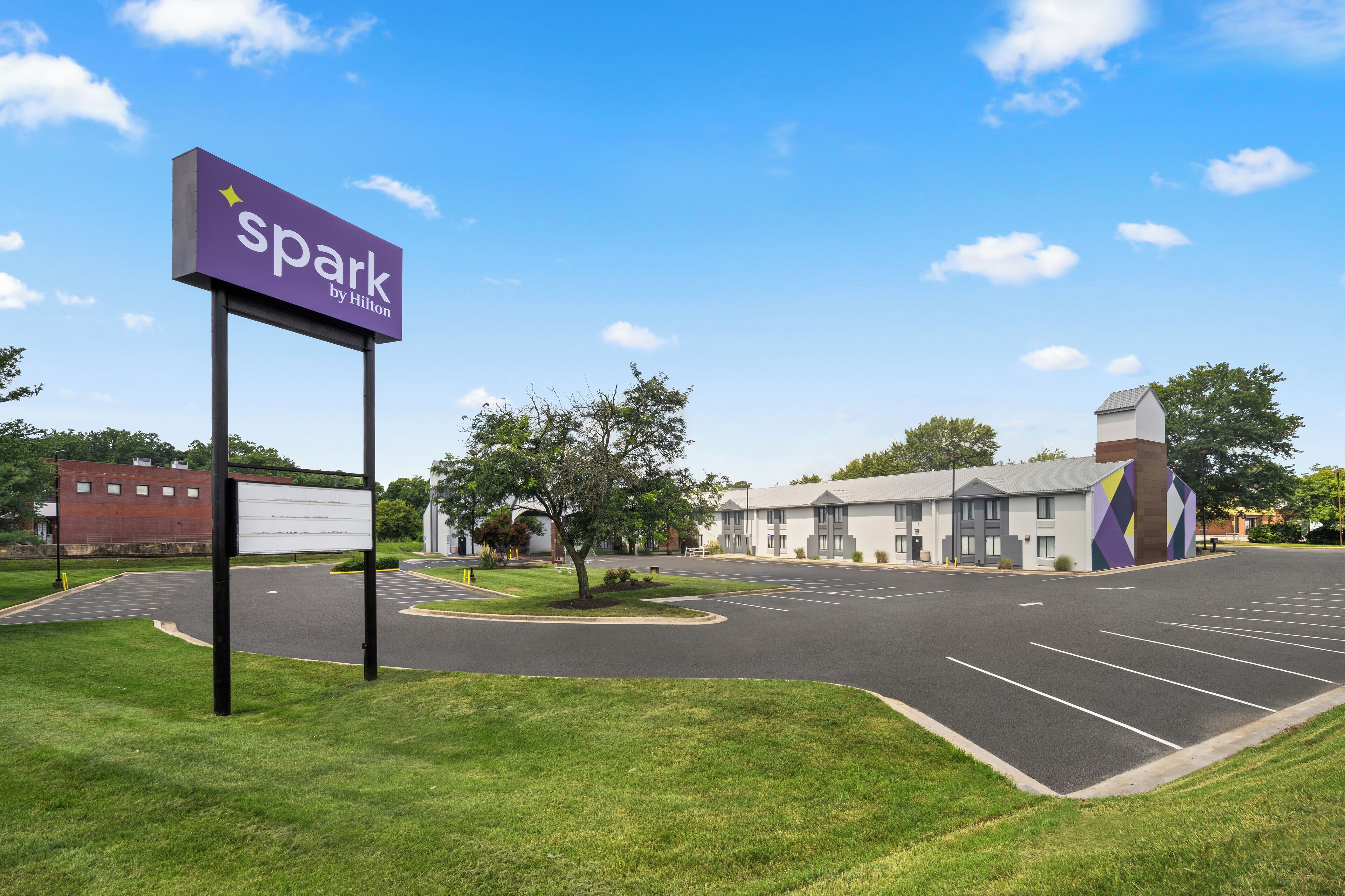 A parking lot with a 'Spark by Hilton' sign, a building with a modern design, and a clear blue sky.