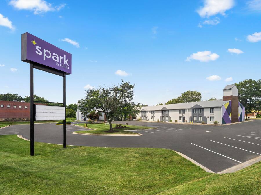 A parking lot with a 'Spark by Hilton' sign, a building with a modern design, and a clear blue sky.
