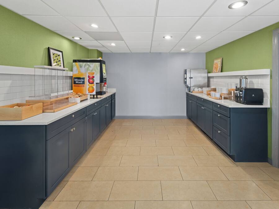 A modern kitchen with dark blue cabinets, white countertops, and green walls. There is a coffee machine, a fruit display, and a coffee maker on the counter.