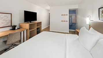 Een moderne hotelkamer met een groot bed, een bureau met een computer, een flatscreen-tv en een zichtbare badkamer door een open deur.