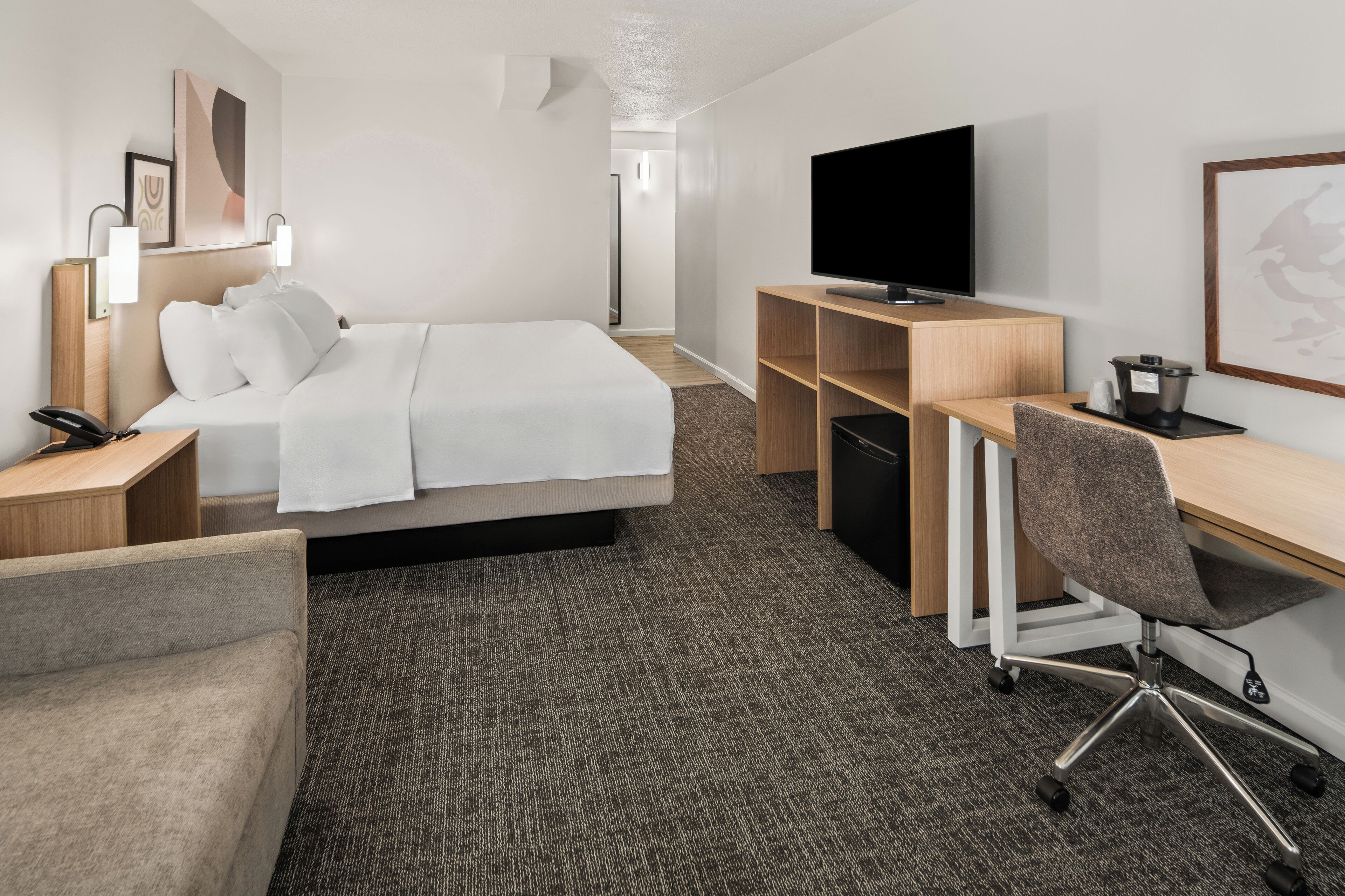 A hotel room with a bed, a desk, a chair, a television, and a telephone.