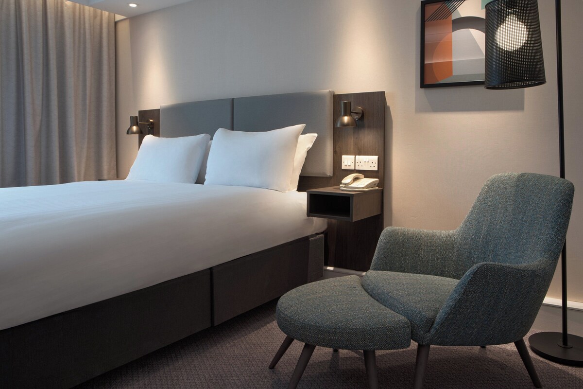 Une chambre d’hôtel moderne dotée d’un grand lit, d’un coin salon, d’un téléphone fixé au mur et d’un luminaire décoratif.
