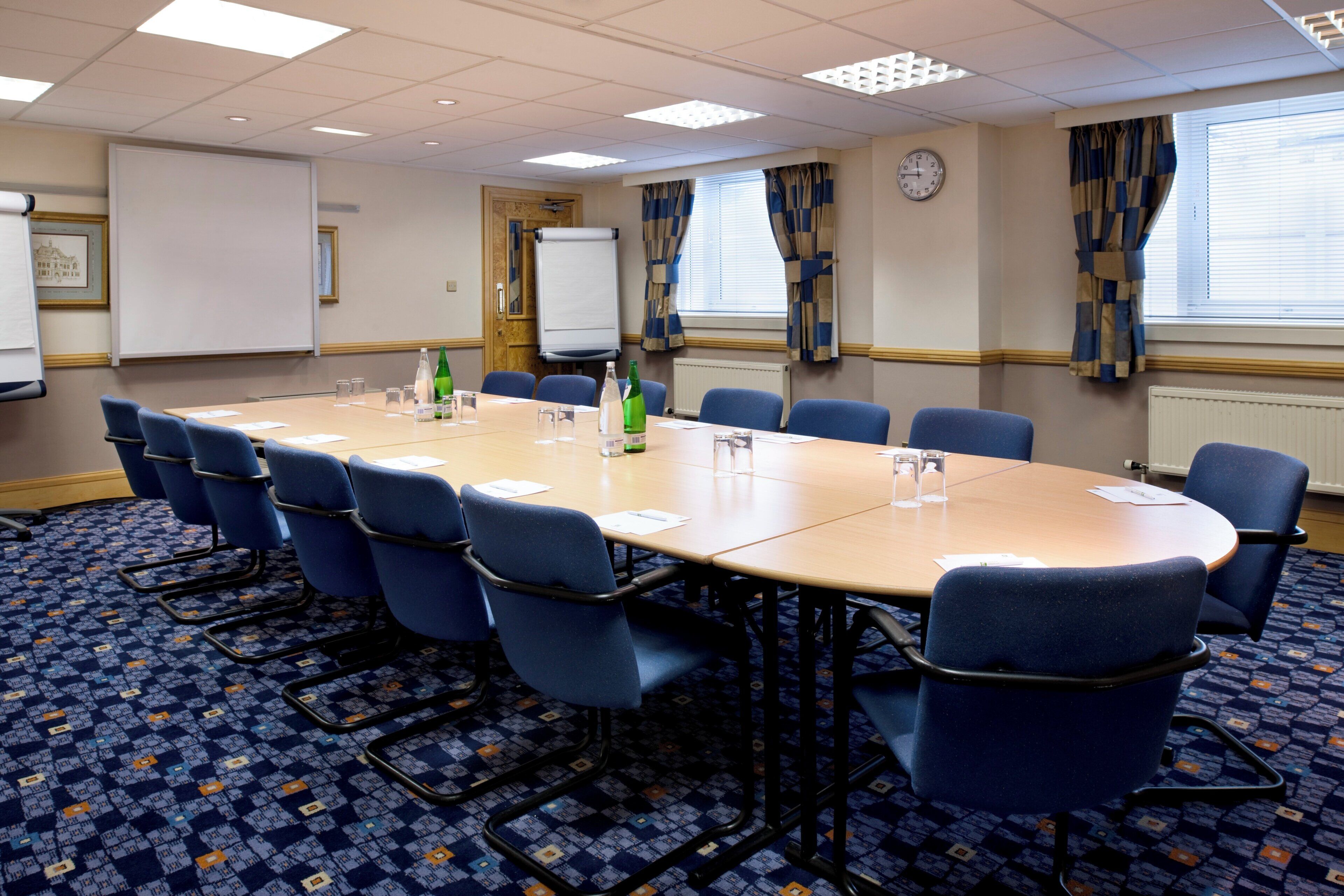 A conference room with a long table, blue chairs, a clock, and a whiteboard.