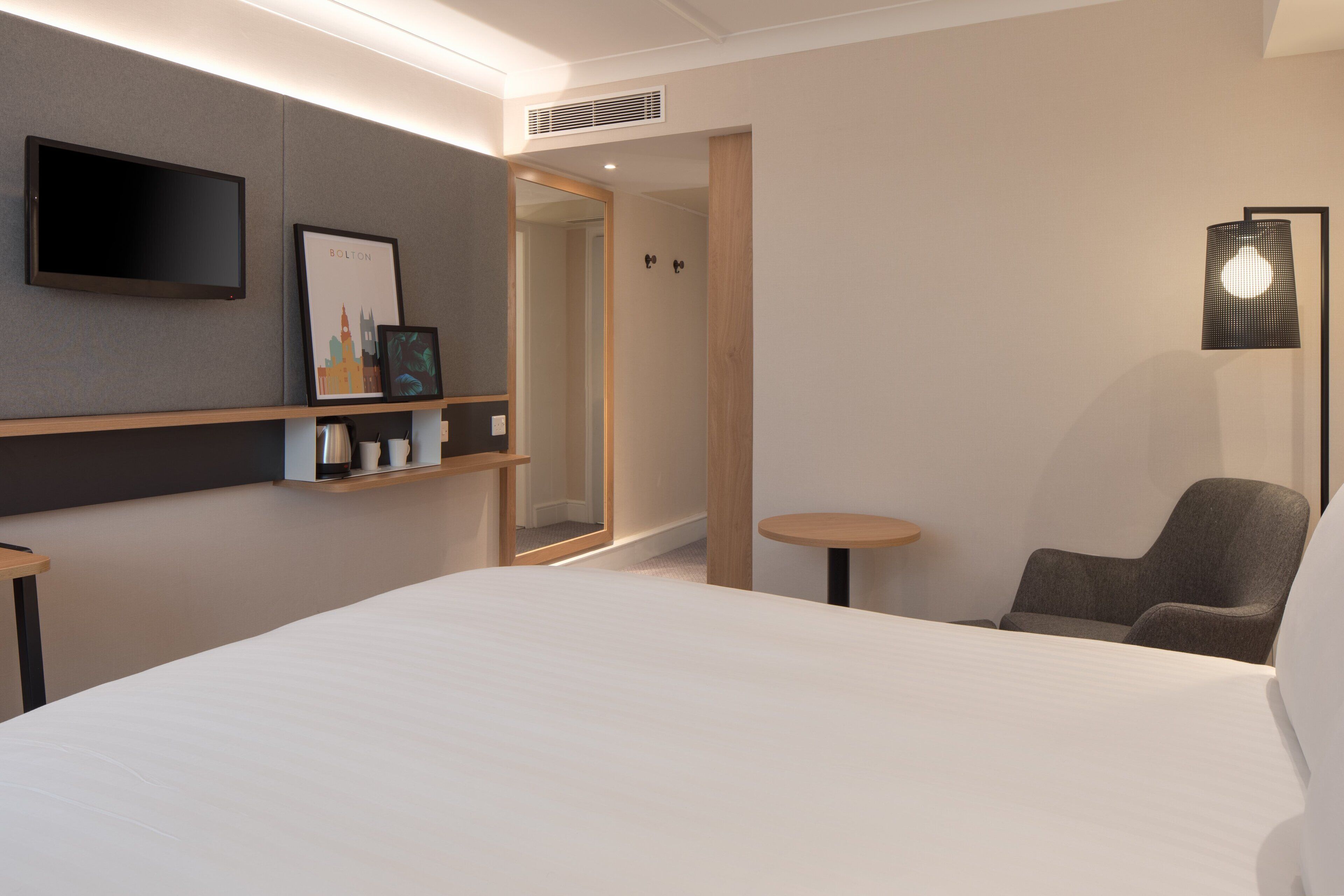 Une chambre d’hôtel moderne avec un grand lit, un téléviseur fixé au mur, un tableau encadré, une petite table et une chaise.