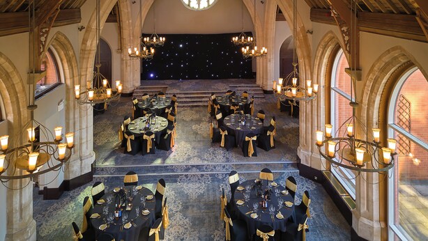 A banquet hall with multiple round tables, chandeliers, and arched ceilings.