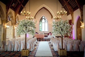 An aisle with chairs and a central aisle leading to a stage, surrounded by chandeliers and floral arrangements.