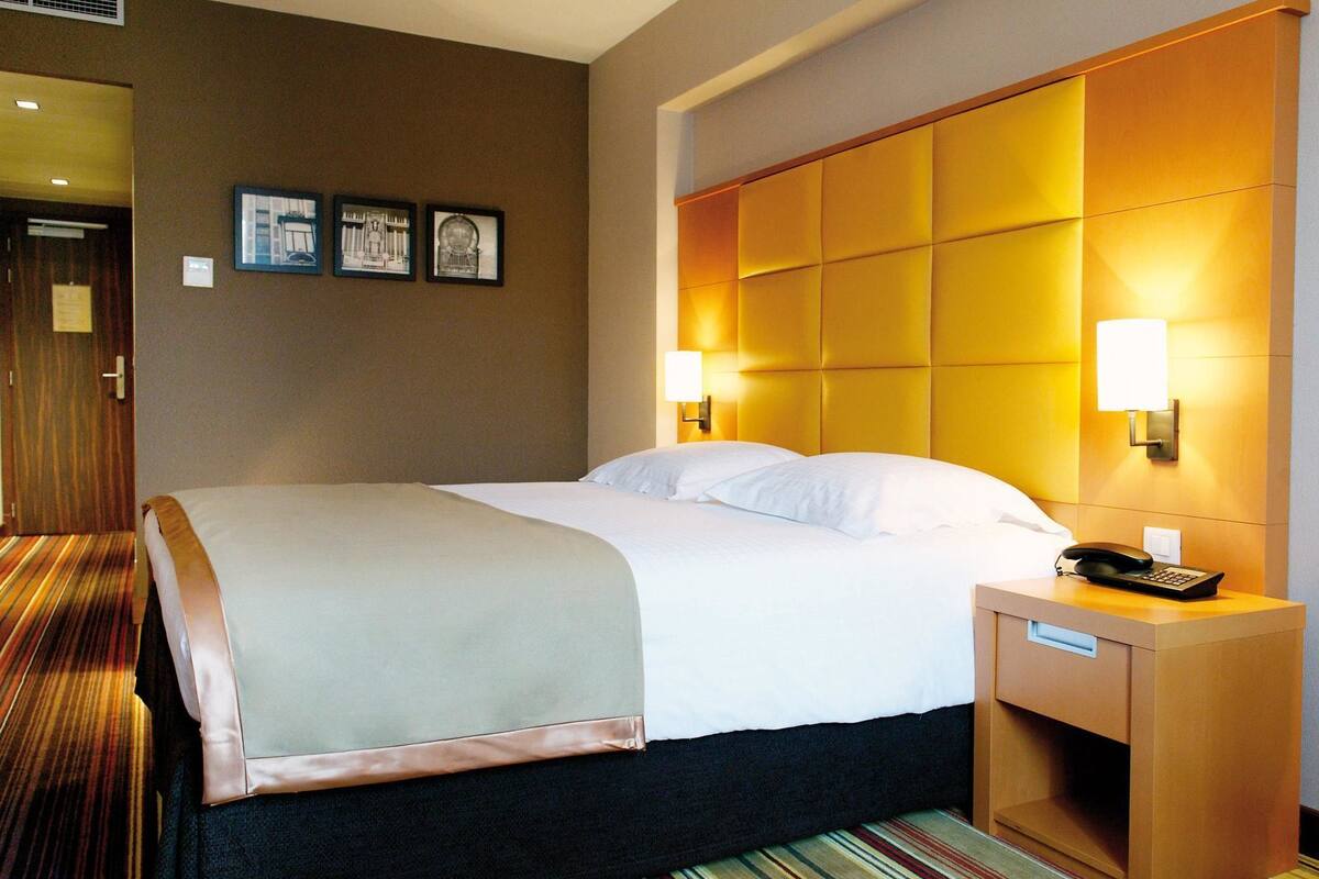 Ein Hotelzimmer mit einem großen Bett, einem Nachttisch mit Telefon und zwei Wandleuchten.