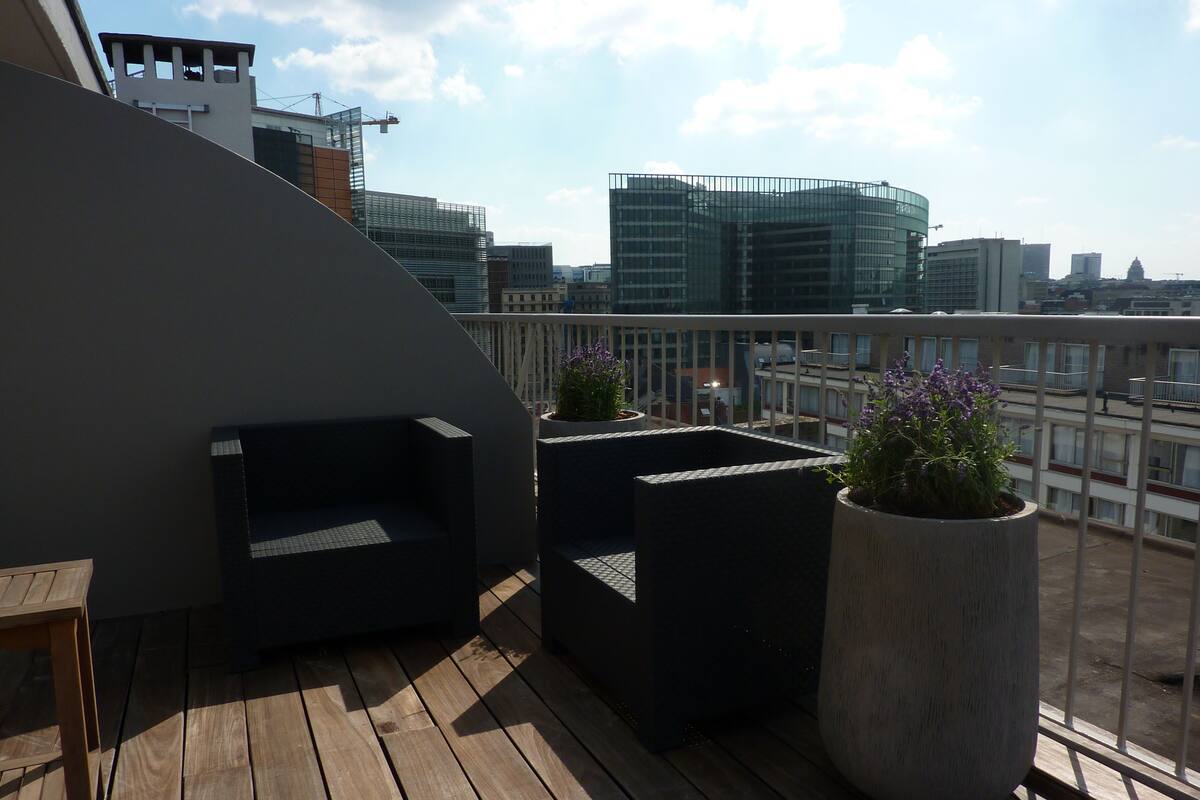 Eine Dachterrasse mit Holzboden, schwarzer Gartenmöbeln und Blumentöpfen.