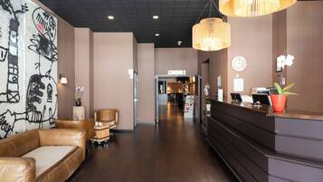 A hotel lobby with a reception desk, seating area, and a hallway leading to meeting rooms.