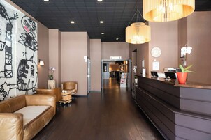Een hotel lobby met een receptiebalie, een zithoek en een gang naar vergaderruimtes.