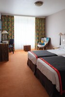Habitación de hotel con dos camas, un escritorio con lámpara, una silla y una ventana con cortinas.