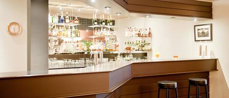 A bar area with a counter, stools, and shelves stocked with bottles and glasses.