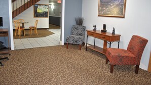 Una habitación con alfombra estampada, un escritorio de madera, una silla, un sillón estampado y un cuadro en la pared.