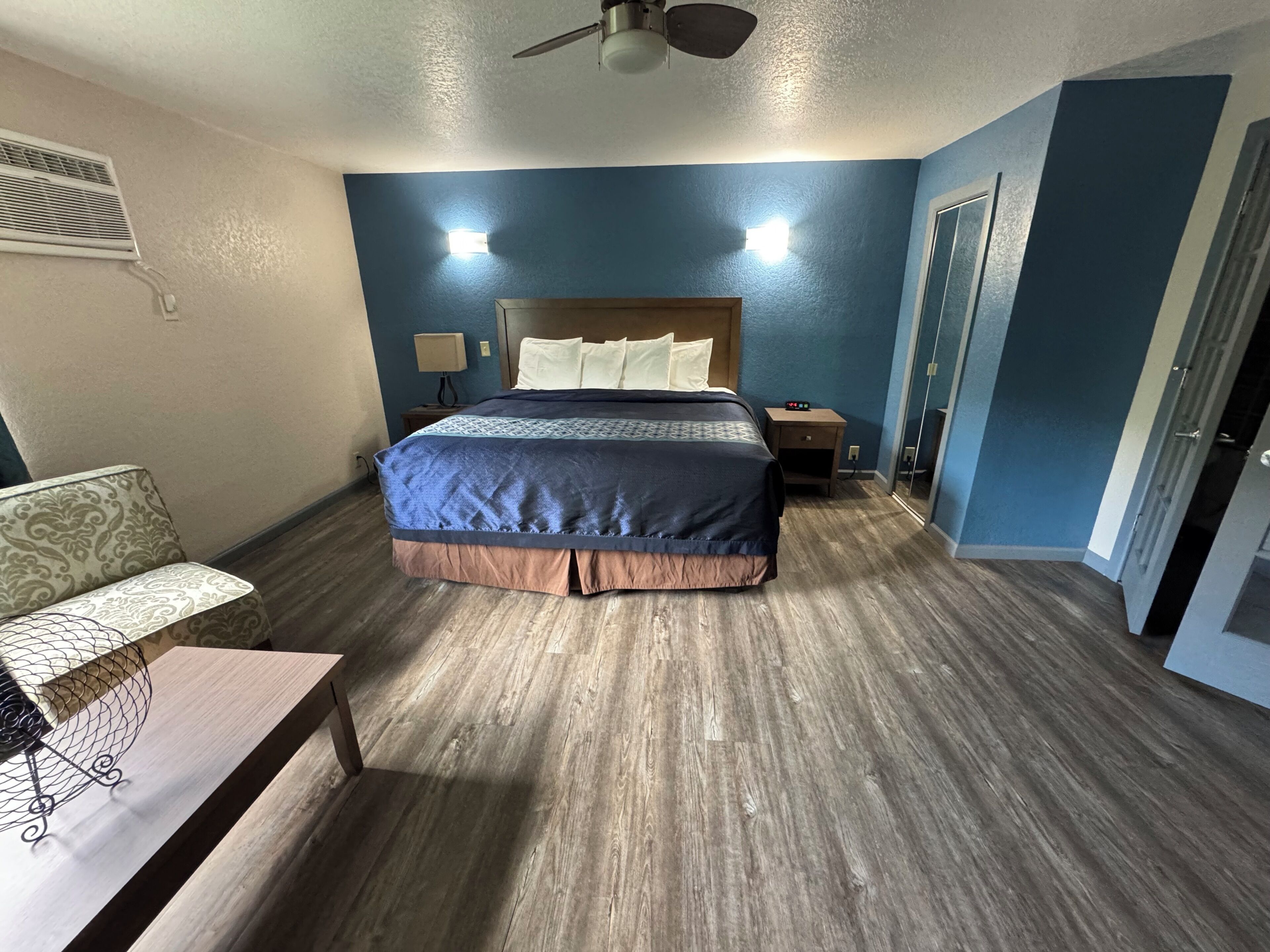 A hotel room with a bed, bedside table, lamp, and a ceiling fan.