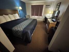 Una habitación de hotel con cama, escritorio, televisor y ventana con cortinas.
