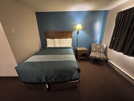Una habitación de hotel con cama, mesita de noche, lámpara, silla y ventana con cortinas.