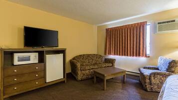 A hotel room with a television, a microwave, a refrigerator, a sofa, a chair, and a small table.
