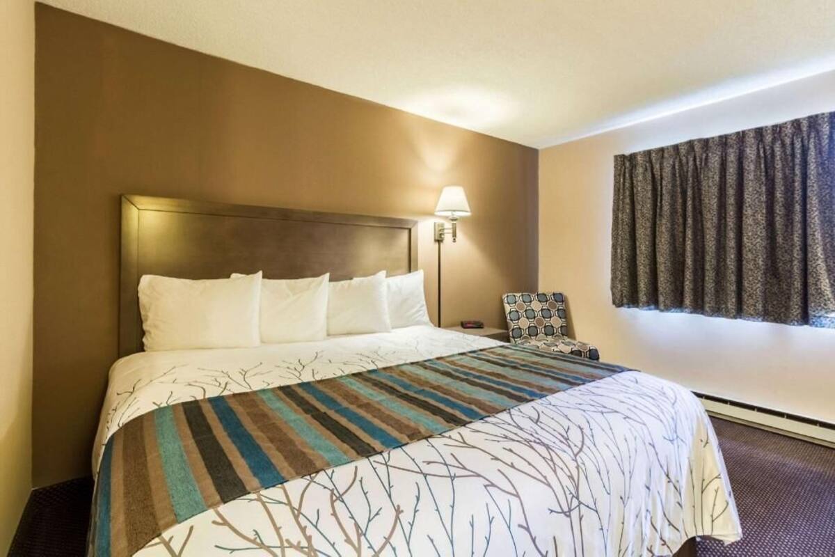 Een hotelkamer met een bed, nachtkastje, lamp en raam met gordijnen.