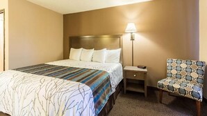 A hotel room with a bed, bedside table, lamp, and patterned armchair. - Red Wing Inn and Suite (Red Wing)