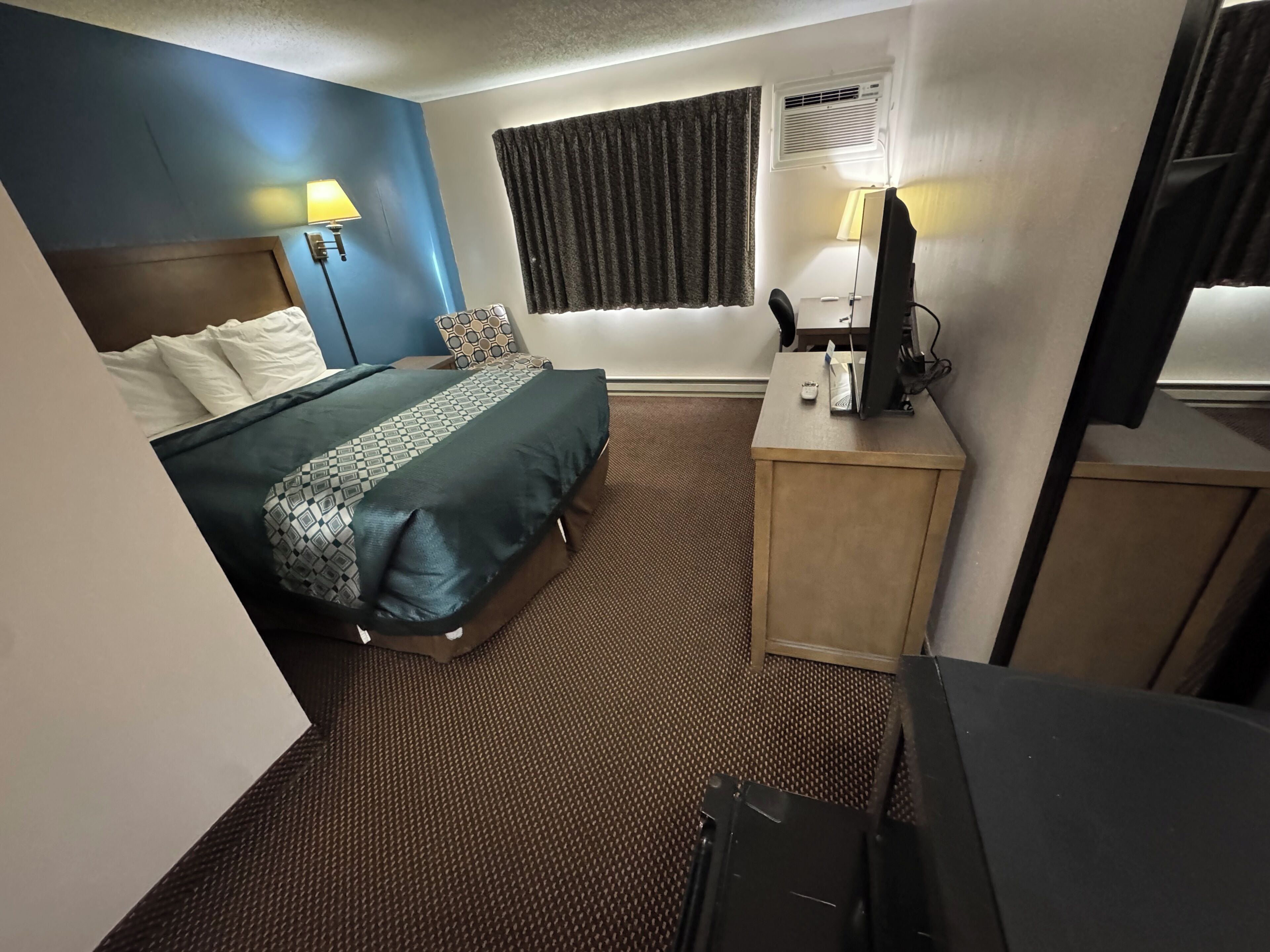 A hotel room with a bed, a desk, a chair, a television, and a window with curtains.