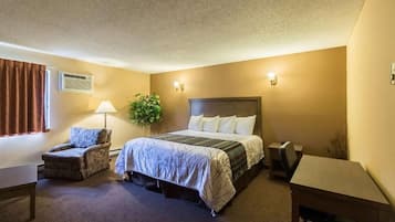 A hotel room with a bed, a desk, a chair, and a plant.