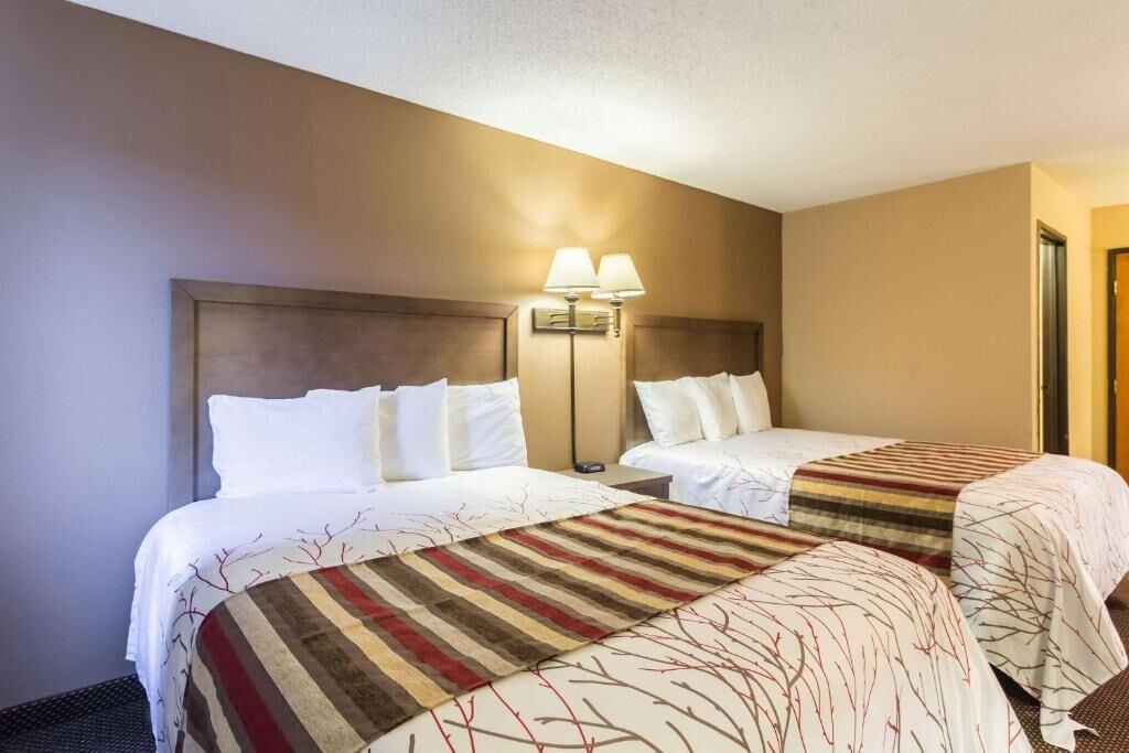 Una habitación de hotel con dos camas, una mesita de noche y una lámpara de pared.
