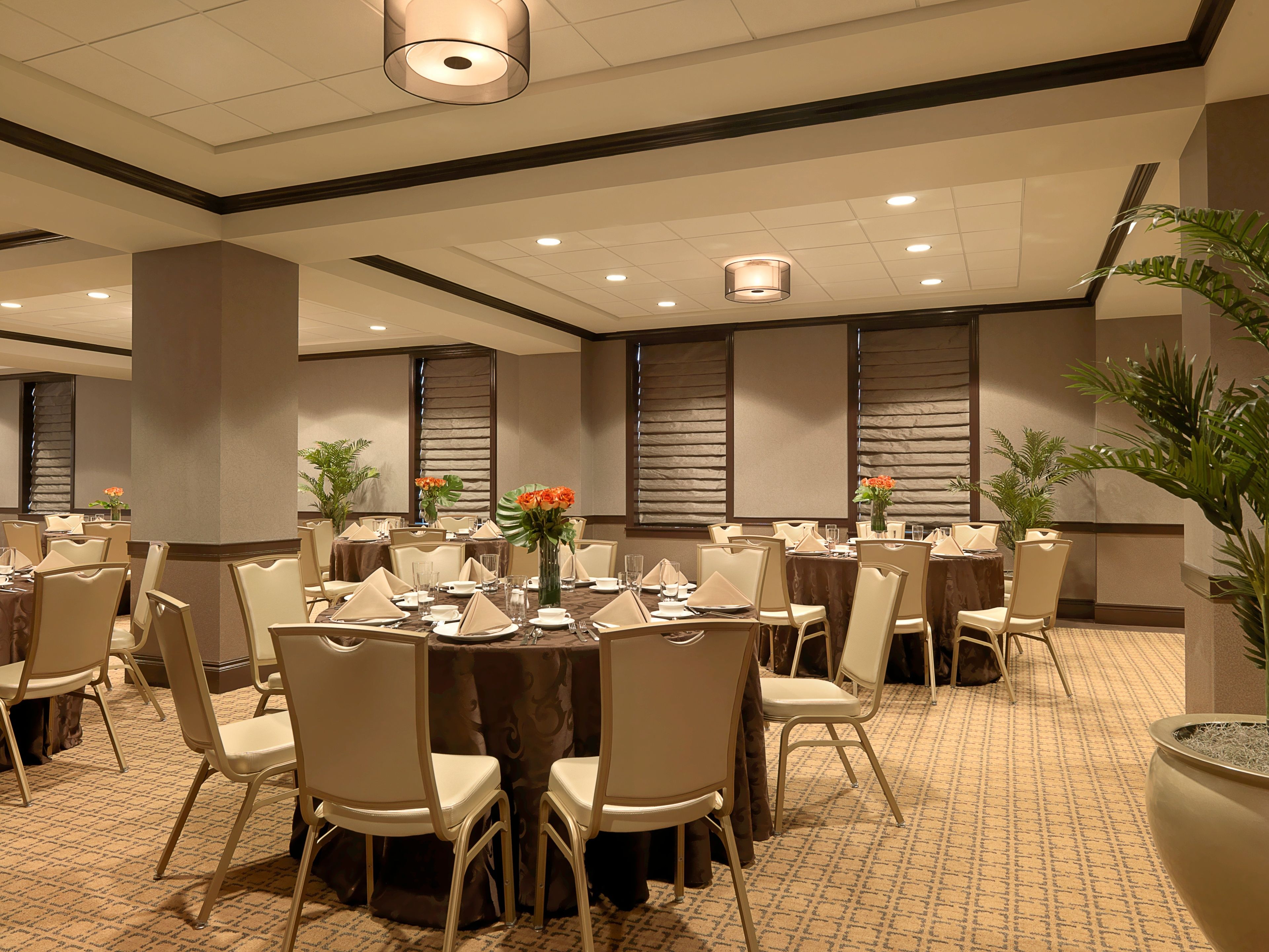 A banquet hall with round tables, chairs, and floral centerpieces.