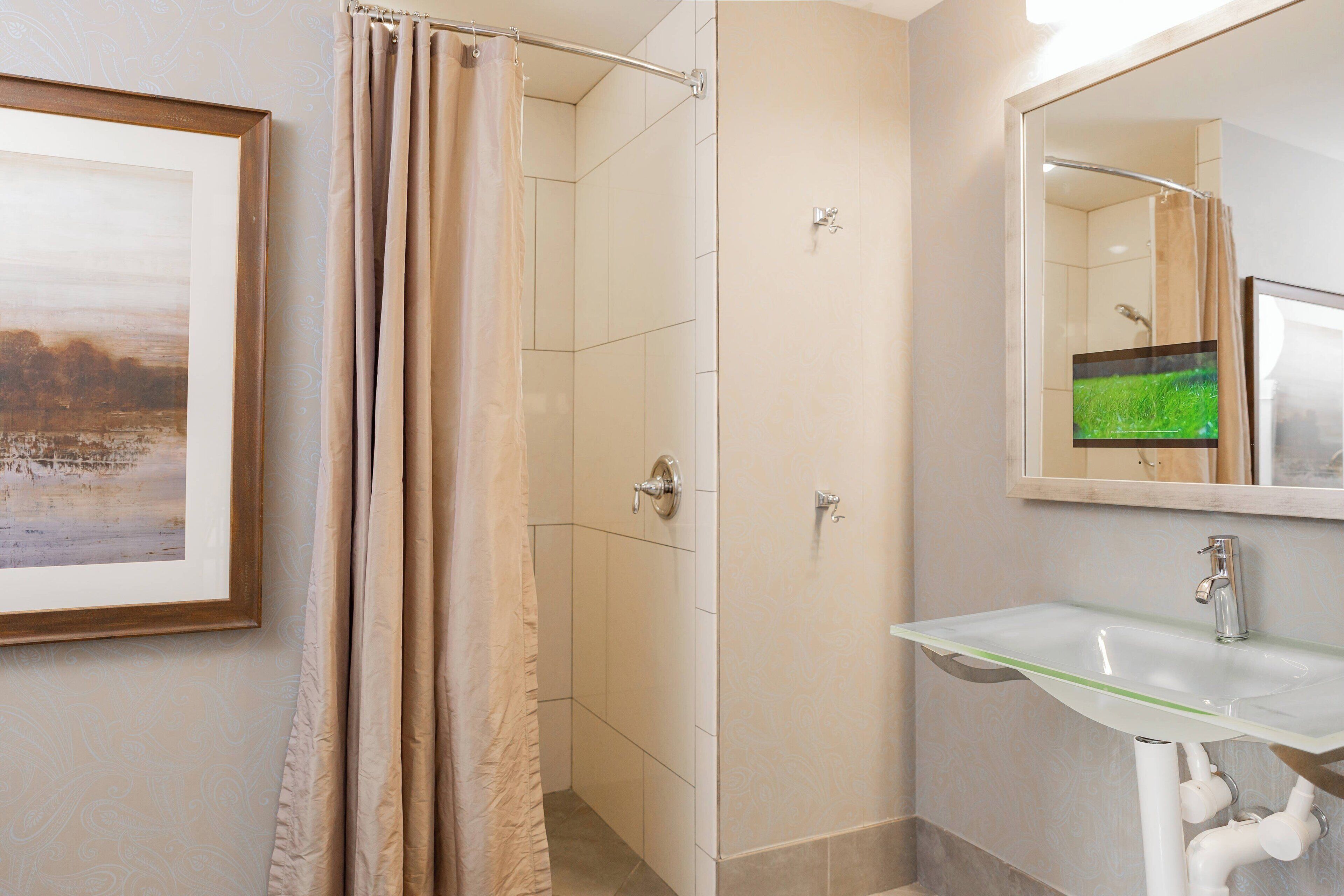 Un baño con un lavamanos de vidrio, una ducha con cortina color beige y un cuadro en la pared.