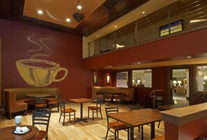 A restaurant with a high ceiling, wooden tables and chairs, a large mural of a steaming cup, and a balcony with a railing. - Hotel Blackhawk, Autograph Collection (Davenport)