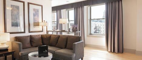 Una sala de estar moderna con un sofá gris, una mesa redonda de centro y una computadora portátil. Hay cuadros enmarcados en la pared, una lámpara y vistas de la ciudad a través de grandes ventanales.