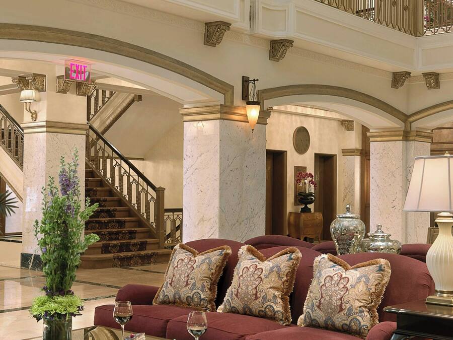 A spacious lobby with a grand staircase, a plush red sofa set, and a chandelier.