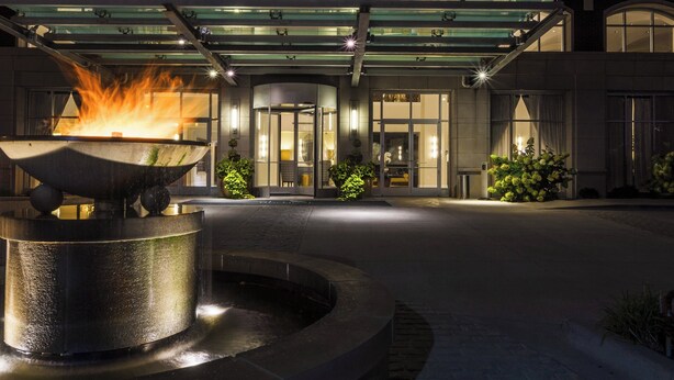 A hotel entrance with a fire feature in the foreground, glass railings, and a well-lit facade. - Hotel Blackhawk, Autograph Collection (Davenport)