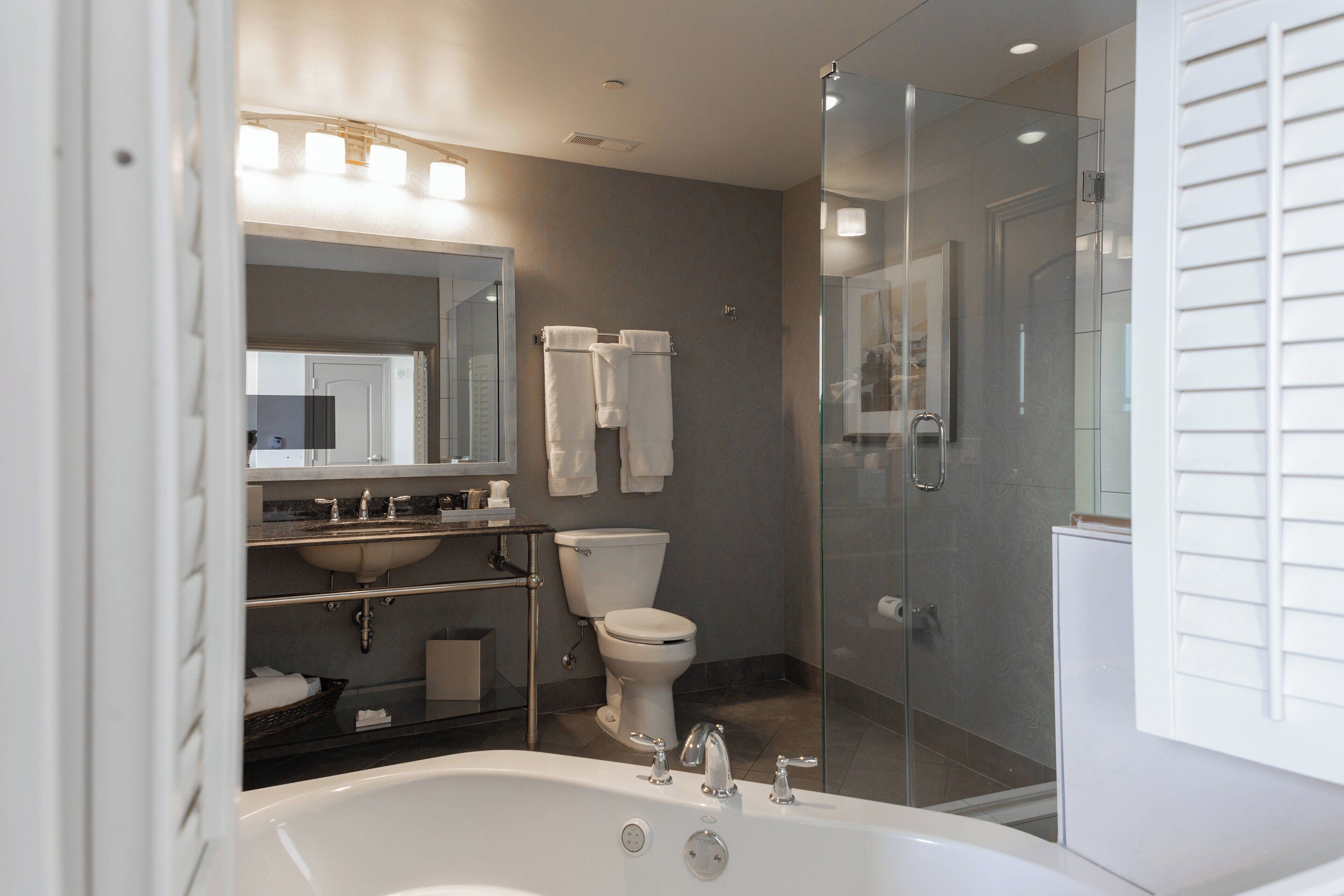 Un baño moderno con ducha de vidrio, una bañera amplia y un tocador con espejo y toallero.