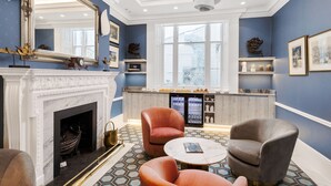 A room with a fireplace, two armchairs, a coffee table, a large mirror, and a bar area with a refrigerator and shelves. - Commodore Hotel (London)