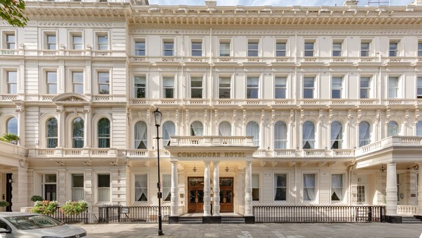 A historic building with a grand entrance labeled "COMMODORE HOTEL." It features multiple windows, a central entrance with columns, and a symmetrical facade. - Commodore Hotel (London)